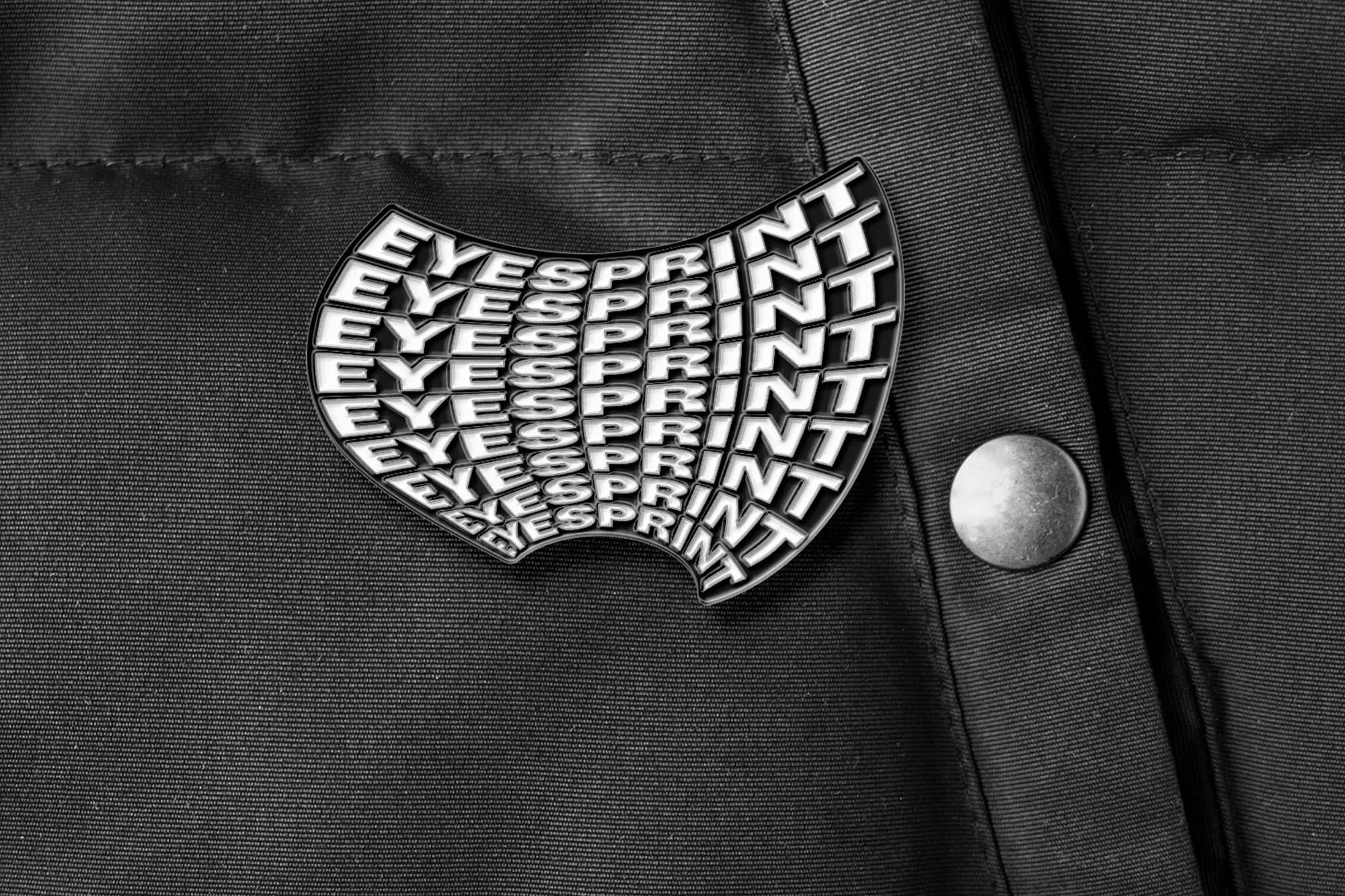 Close-up of a jacket featuring a pin with the word 'Eyesprint' repeated in a distorted, curved pattern, emphasizing a modern and edgy style.