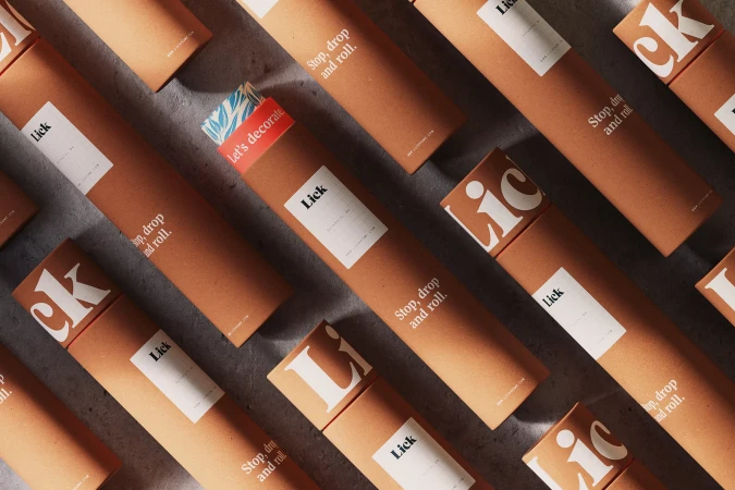 Multiple brown cardboard tubes with the brand name 'Lick' and white labels scattered across a textured gray surface, creating a pattern.