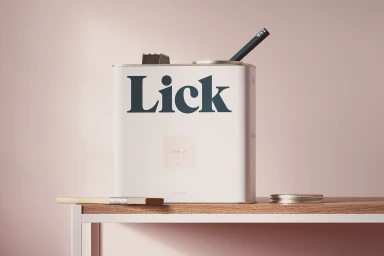 White Lick paint tin with bold dark lettering sitting on a wooden surface against a pale pink background
