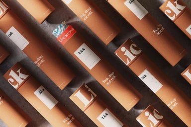 An overhead arrangement of brown cardboard packaging tubes with white branding labels on a dark textured concrete surface.
