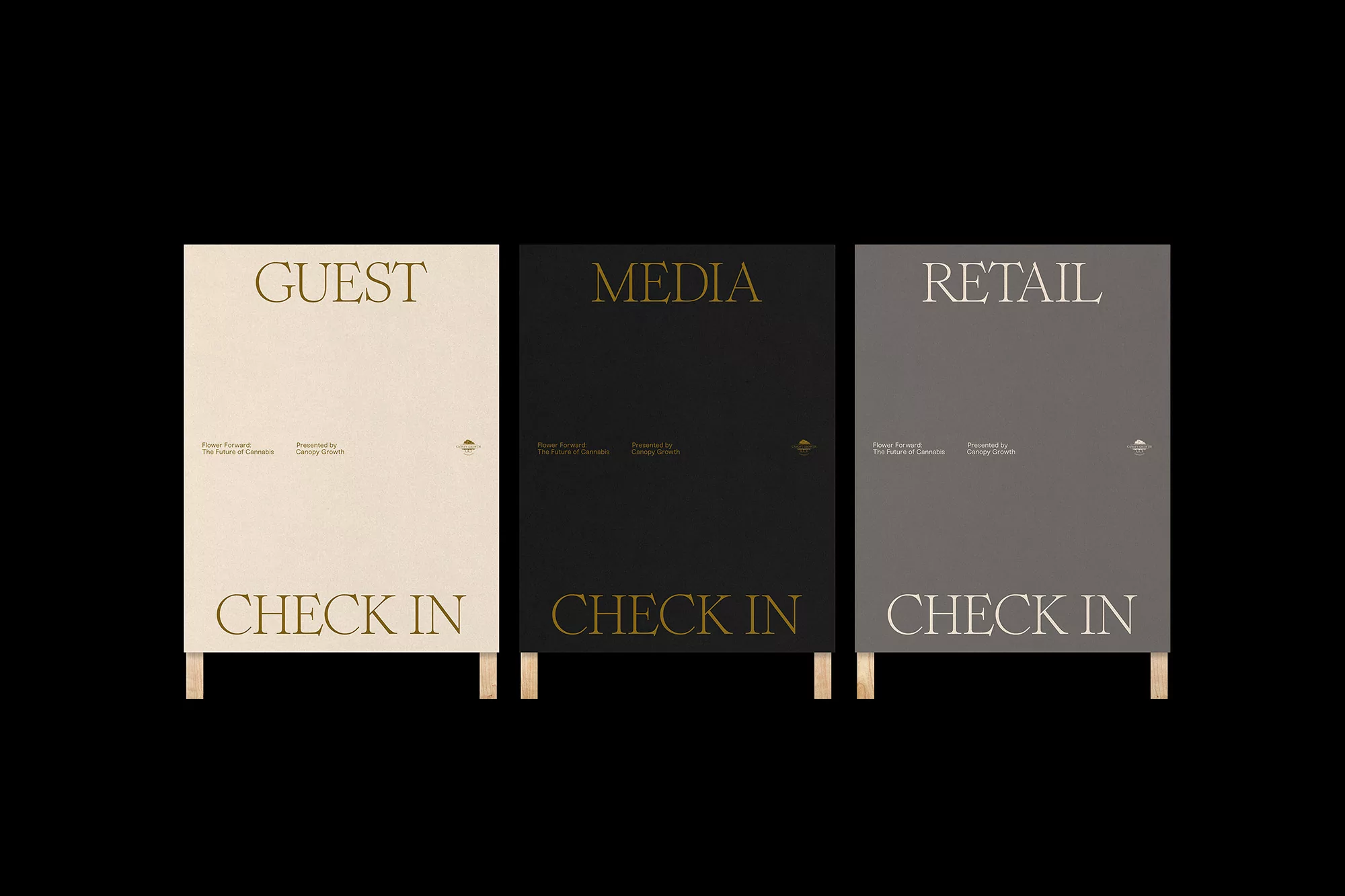 Three signs in black, white, and grey, on wood legs, read: Guest Check In, Media Check In, and Retail Check In on a black background.