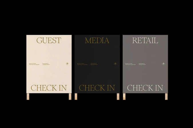Three signs in black, white, and grey, on wood legs, read: Guest Check In, Media Check In, and Retail Check In on a black background.