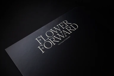 Black printed card featuring white serif typography reading FLOWER FORWARD on a dark surface