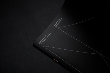 Close-up angled shot of a dark black booklet featuring minimalist white geometric lines and typography text.