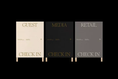 Three vertical signage boards with serif typography reading GUEST CHECK IN, MEDIA CHECK IN, and RETAIL CHECK IN against a black background.