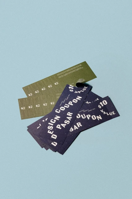 Graphic design coupons in shades of olive green and navy blue scattered on a powder-blue surface, showcasing promotional offers.