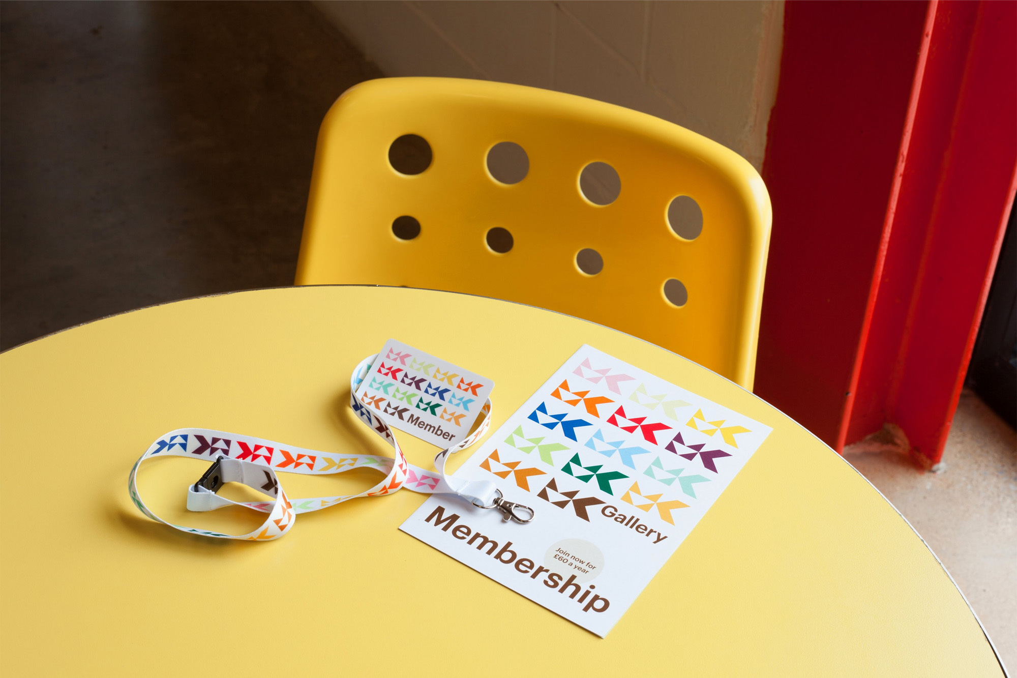 Close-up of a yellow table with a yellow chair, showcasing a membership card and lanyard with colorful geometric patterns in an indoor setting.