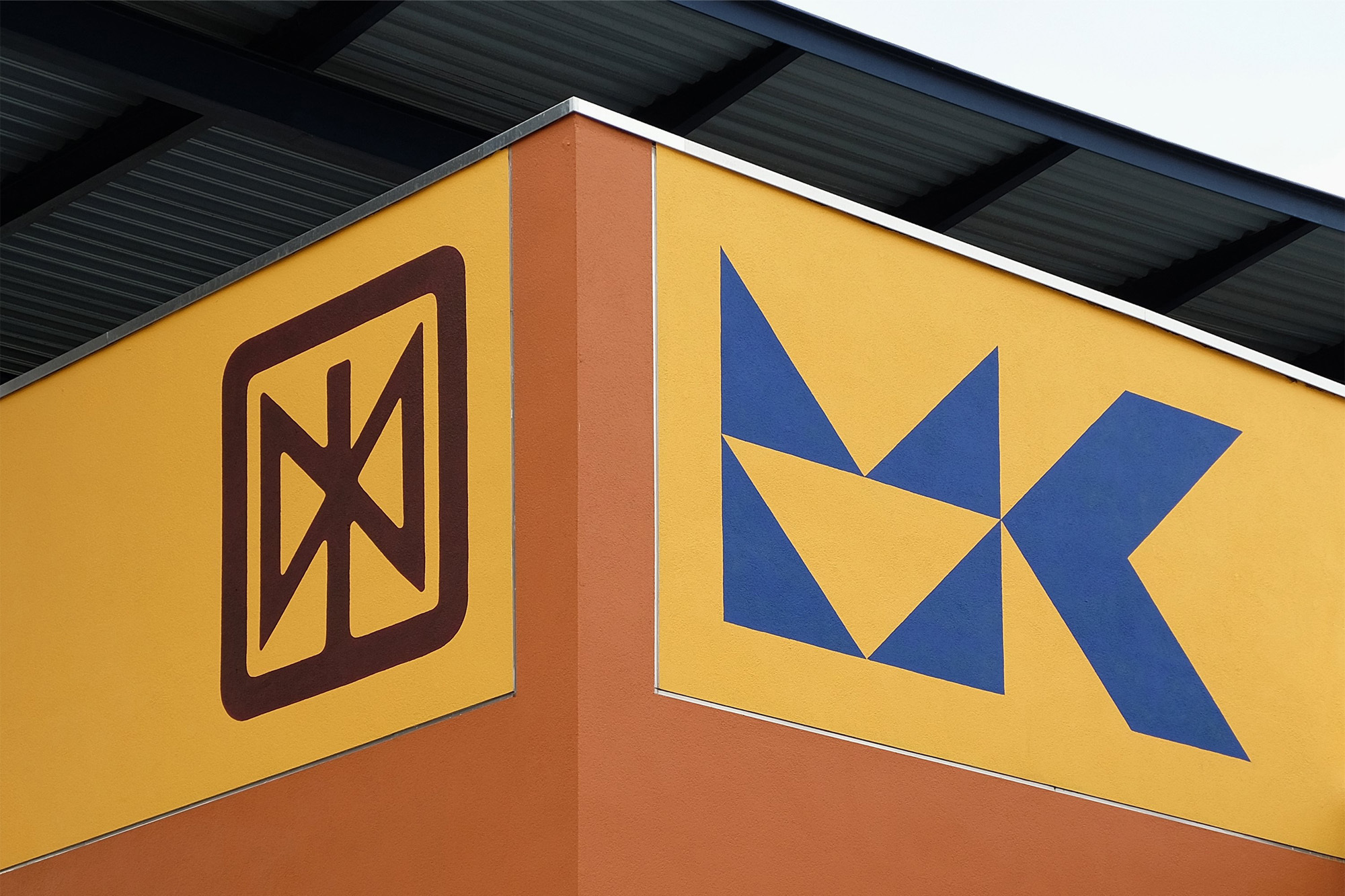 Exterior view of a building with geometric symbols and shapes painted on the wall in shades of brown, blue, and yellow.