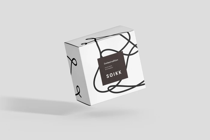 A white branded packaging box featuring black line art graphics and a dark central label against a seamless light background.