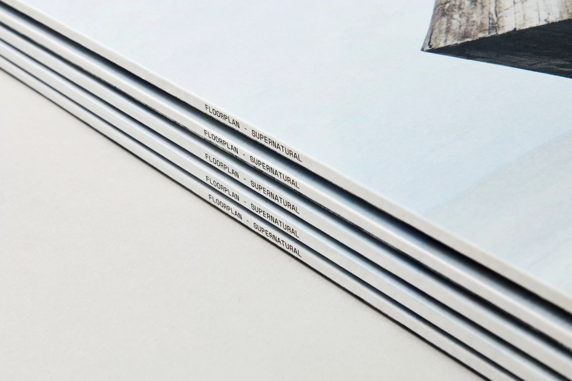 Close-up of four stacked books with the title 'FLOORPLAN - SUPERNATURAL' printed on their spines, creating a minimalist, abstract composition.