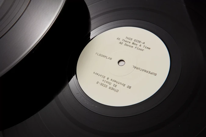 High-angle close-up of a black vinyl record with a cream-colored label displaying the album title, tracklist, and artist in black text.