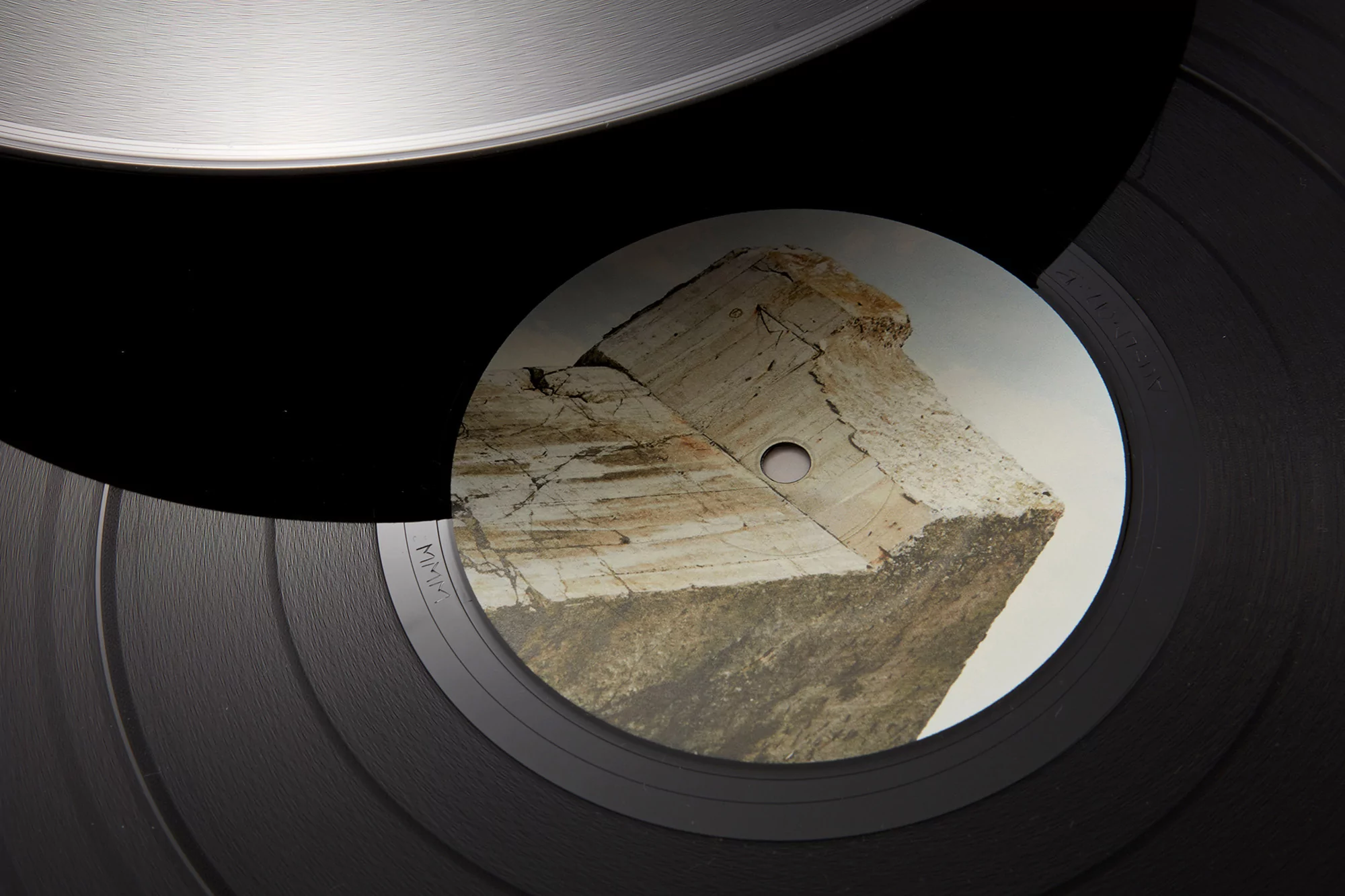 Vinyl record with a geological cube design on the label. Music album artwork with a rock formation, set against the black vinyl backdrop.