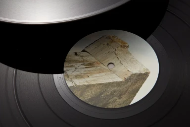 Close-up of a vinyl record being lifted, revealing a label featuring a textured stone graphic on the black record surface.