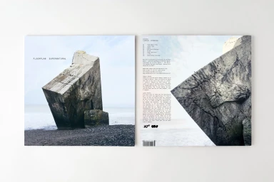 Vinyl record album cover design featuring a concrete block on a pebble beach with typography on a white background