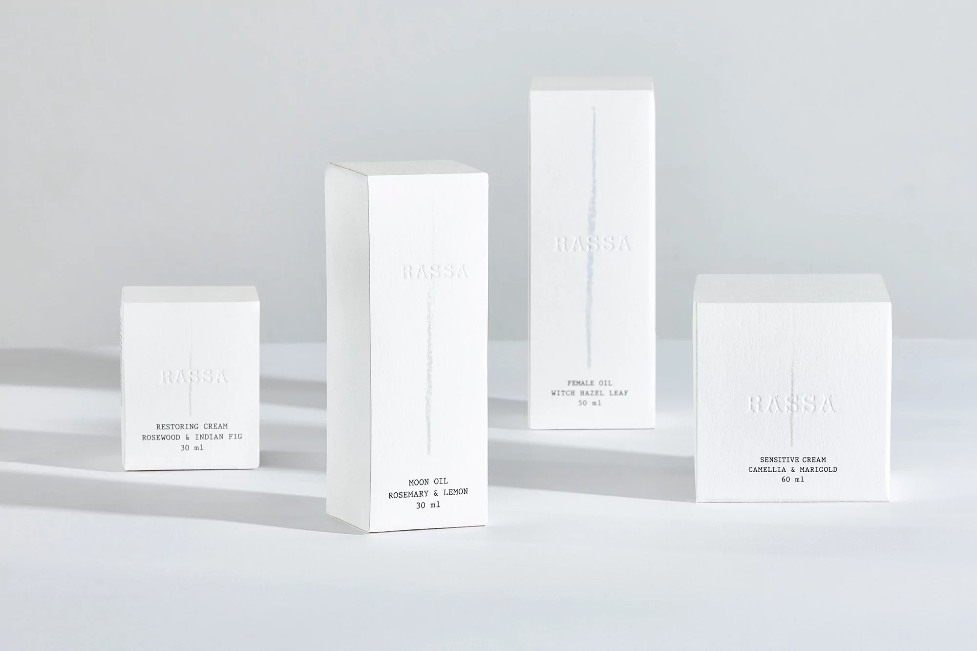 Four white boxes of BASSA skincare products sit in a bright studio setting with visible text on each box indicating different creams and oils.