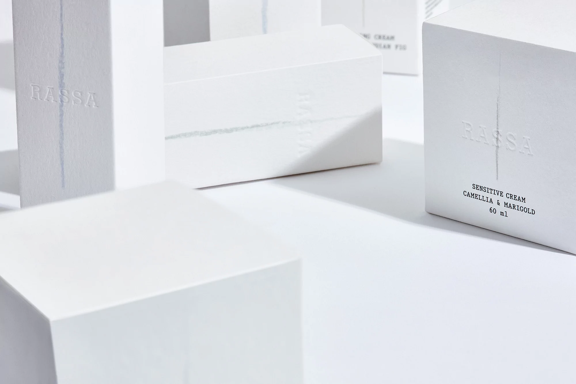 Still life of white Rassa skin cream boxes in studio. Minimalist beauty product packaging in geometric shapes against a white background.