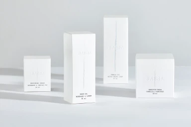 Four minimalist white skincare product boxes arranged on a pale grey surface casting soft shadows.