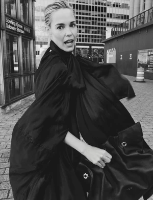 Leslie Bibb in black coat holding leather handbag on urban street near subway station