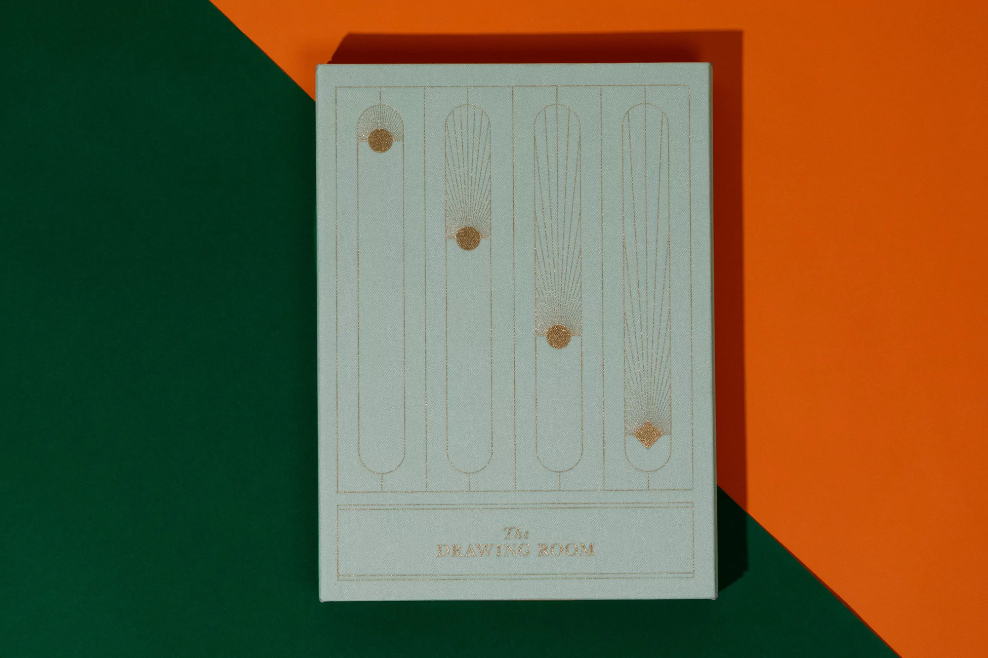 Close-up of a light blue book with an art deco design in gold ink featuring vertical lines and dots against an orange and green background.