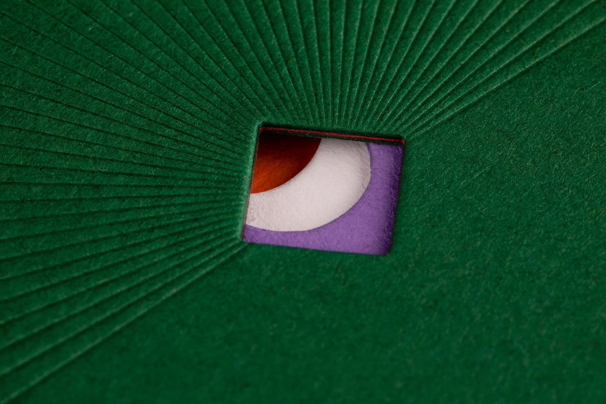Abstract image showcasing a green textured surface with a square cutout revealing layered colors of orange, white, and purple.