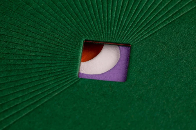 Abstract image showcasing a green textured surface with a square cutout revealing layered colors of orange, white, and purple.