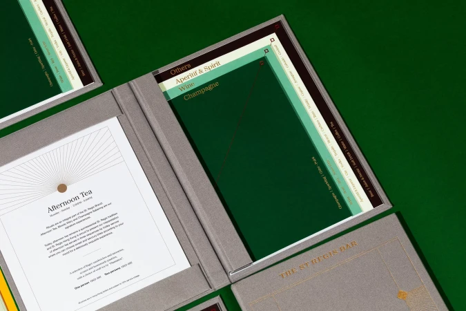 High-angle shot of open menus displaying drink selections and afternoon tea options, presented on a vibrant green surface.
