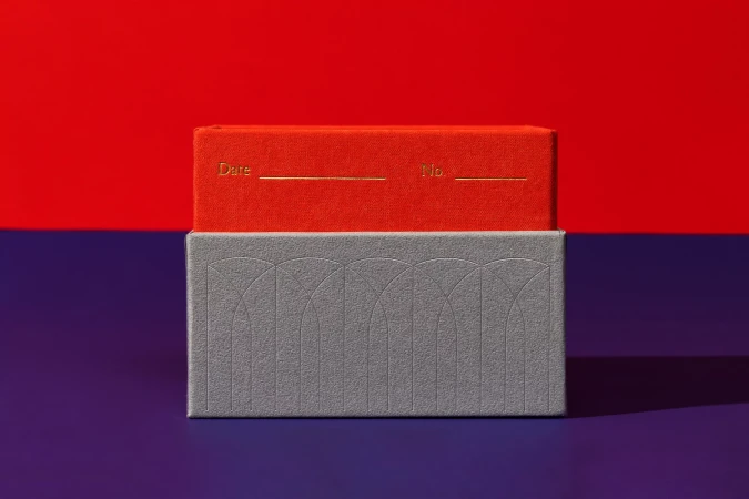 A red book resting on top of a textured grey box against a red and purple studio background.