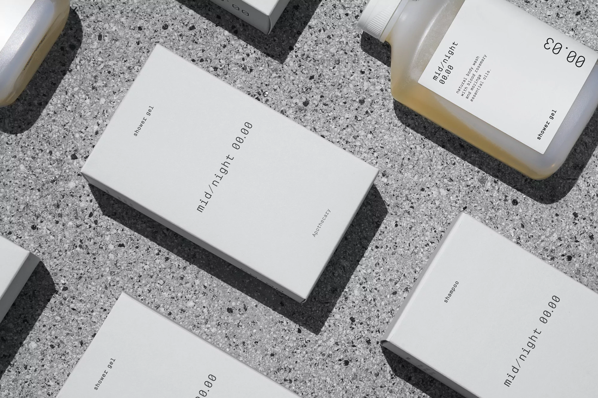 Several white boxes and a bottle of gel or shampoo are arranged on a gray speckled surface, with the brand name mid/night 00.00 visible.