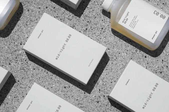 Several white boxes and a bottle of gel or shampoo are arranged on a gray speckled surface, with the brand name mid/night 00.00 visible.