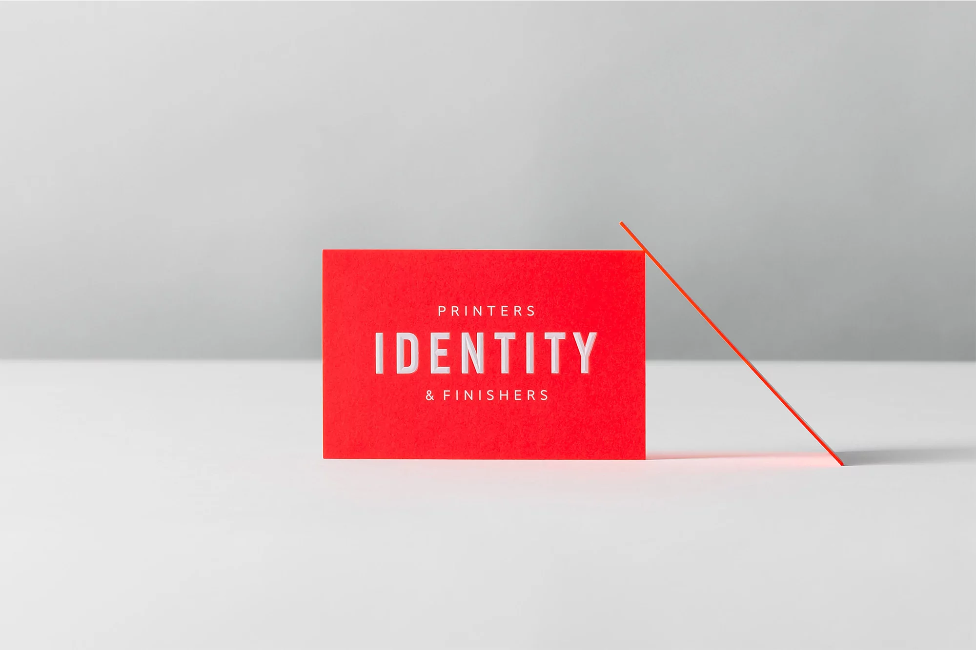 Close-up of a vibrant red business card displaying the text 'PRINTERS IDENTITY & FINISHERS' in white against a minimalist backdrop.
