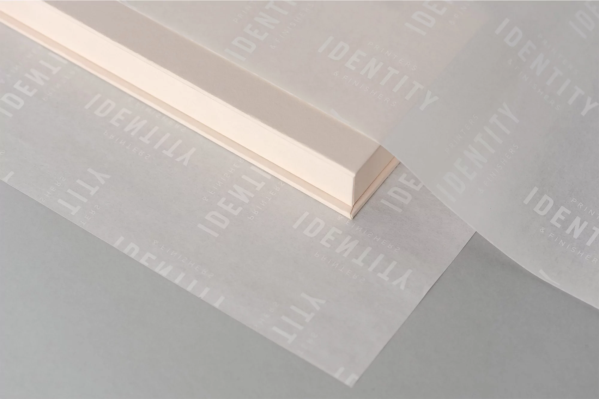 Minimalist product shot featuring a cream-colored box with clean lines, overlaid with translucent paper printed with a repeating logo.