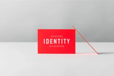 Red business card featuring embossed white text resting on a smooth grey surface against a white backdrop