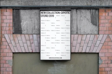 Vertical advertising poster mounted on a textured brick and concrete wall, displaying bold typographic text.