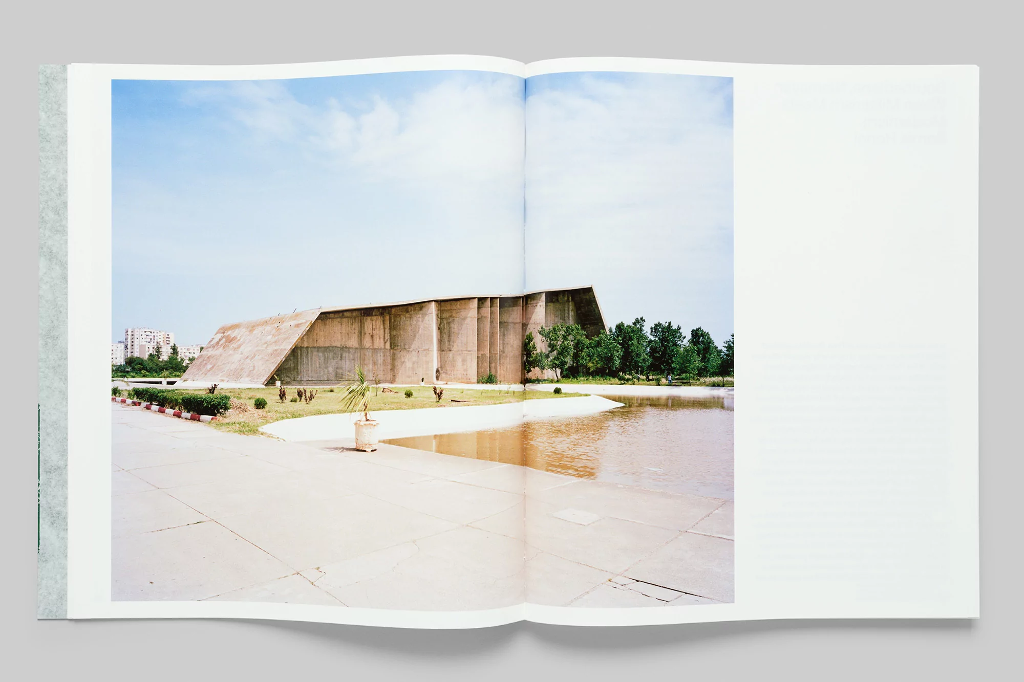Architectural photo of an institutional building next to a reflective pond, set in a book against a clear blue sky and urban backdrop.