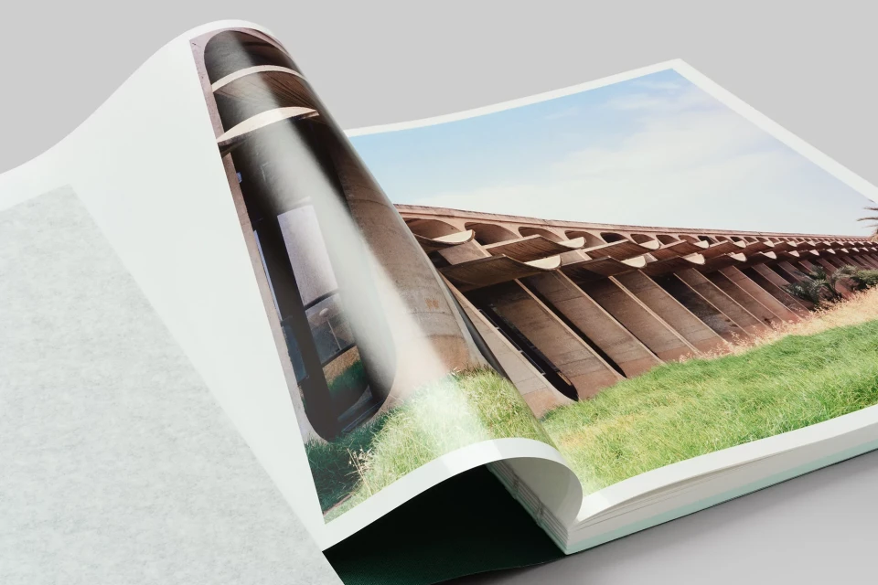 Opened book shows a concrete structure with arches over grass under a clear sky, with book pages partially obscuring the scene.