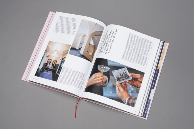 An open hardcover book showing interior pages with photographs, text blocks, and architectural imagery against a plain grey background.