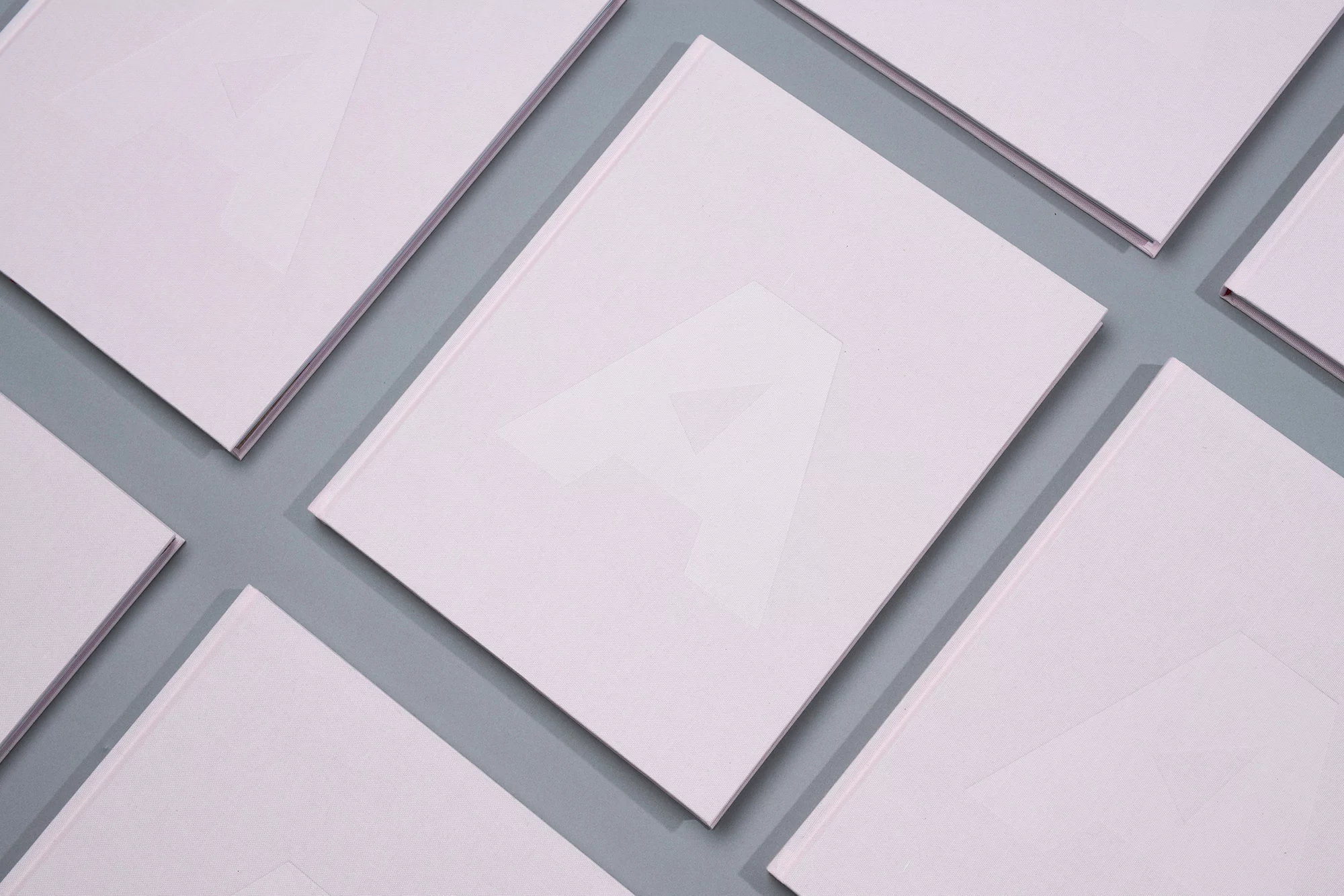 Several closed, light pink hardcover books are arranged on a flat, light grey surface in a studio product shot.