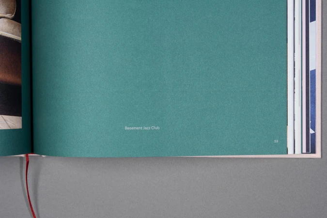 Open book with textured teal page featuring the text 'Basement Jazz Club', surrounded by other pages with hints of imagery.