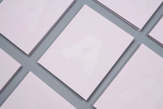 Multiple pale pink books featuring a debossed letter A on the cover arranged in a neat grid on a grey surface.
