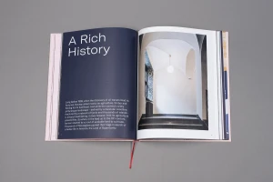 An open book on a grey surface displaying dark blue pages with white text and an architectural photography spread on the right page.