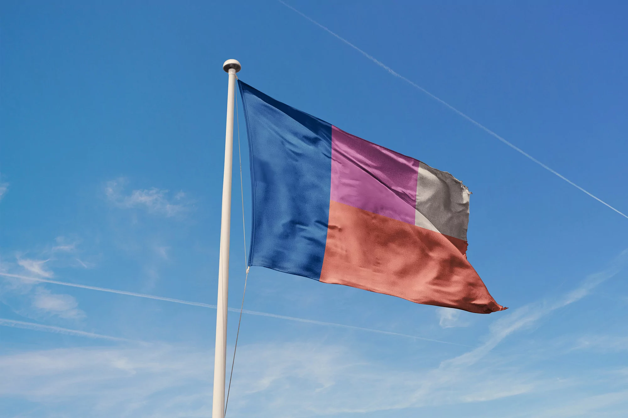 A colorful flag with a blue, pink, brown and grey color block design waving against a bright blue sky with contrails visible above.