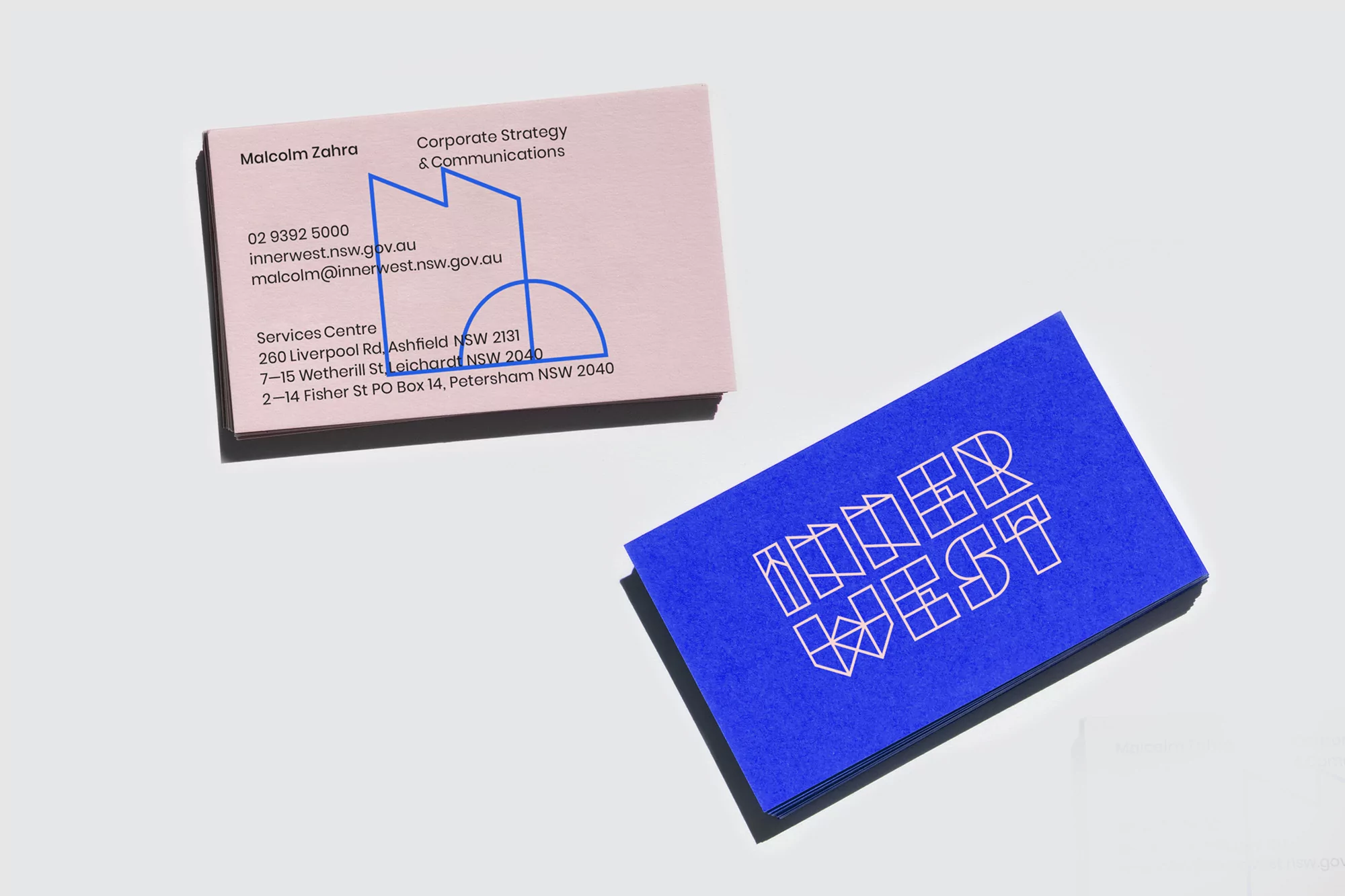 Two business cards on a white surface, one pink with contact information and blue geometric design, and one blue with white text.