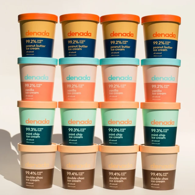 Stacked tubs of Denada ice cream in assorted flavors: peanut butter, vanilla, mint chip, and double chocolate, creating a vibrant dessert display.