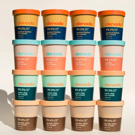 Stacked tubs of Denada ice cream in assorted flavors: peanut butter, vanilla, mint chip, and double chocolate, creating a vibrant dessert display.
