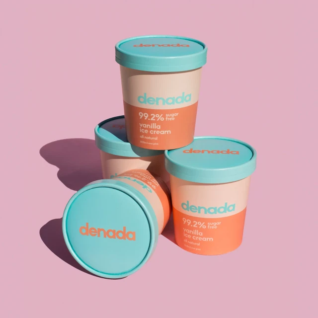 Stack of Denada brand vanilla ice cream pints with light blue lids, arranged against a light pink background in a studio setting.