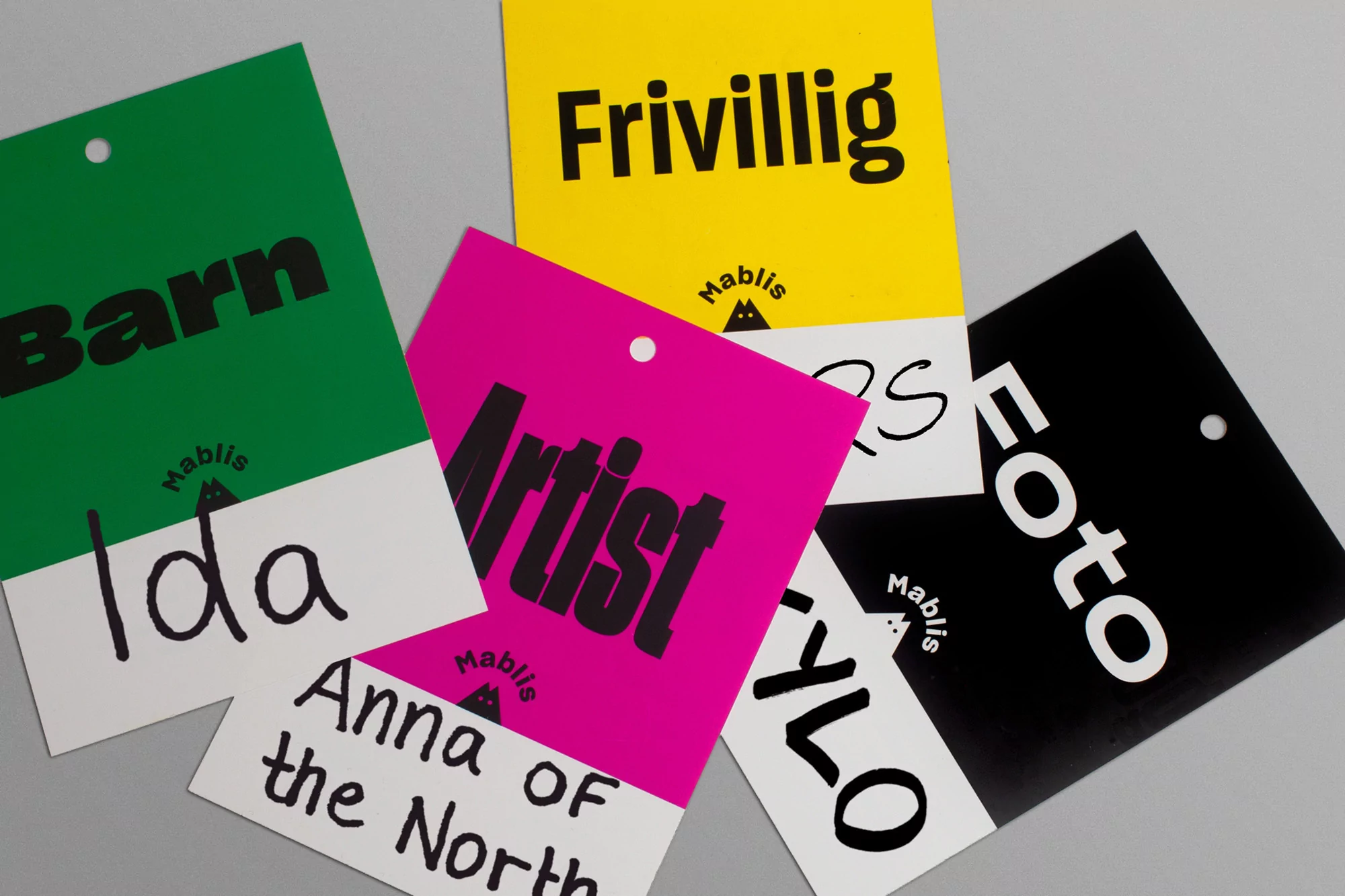 Colorful paper tags with various words like 'Barn,' 'Artist,' and 'Foto' arranged on a gray surface in a studio setting. 