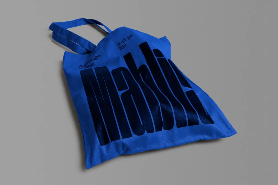 Blue tote bag on a gray surface featuring black stylized text, with a clean, minimalist aesthetic.