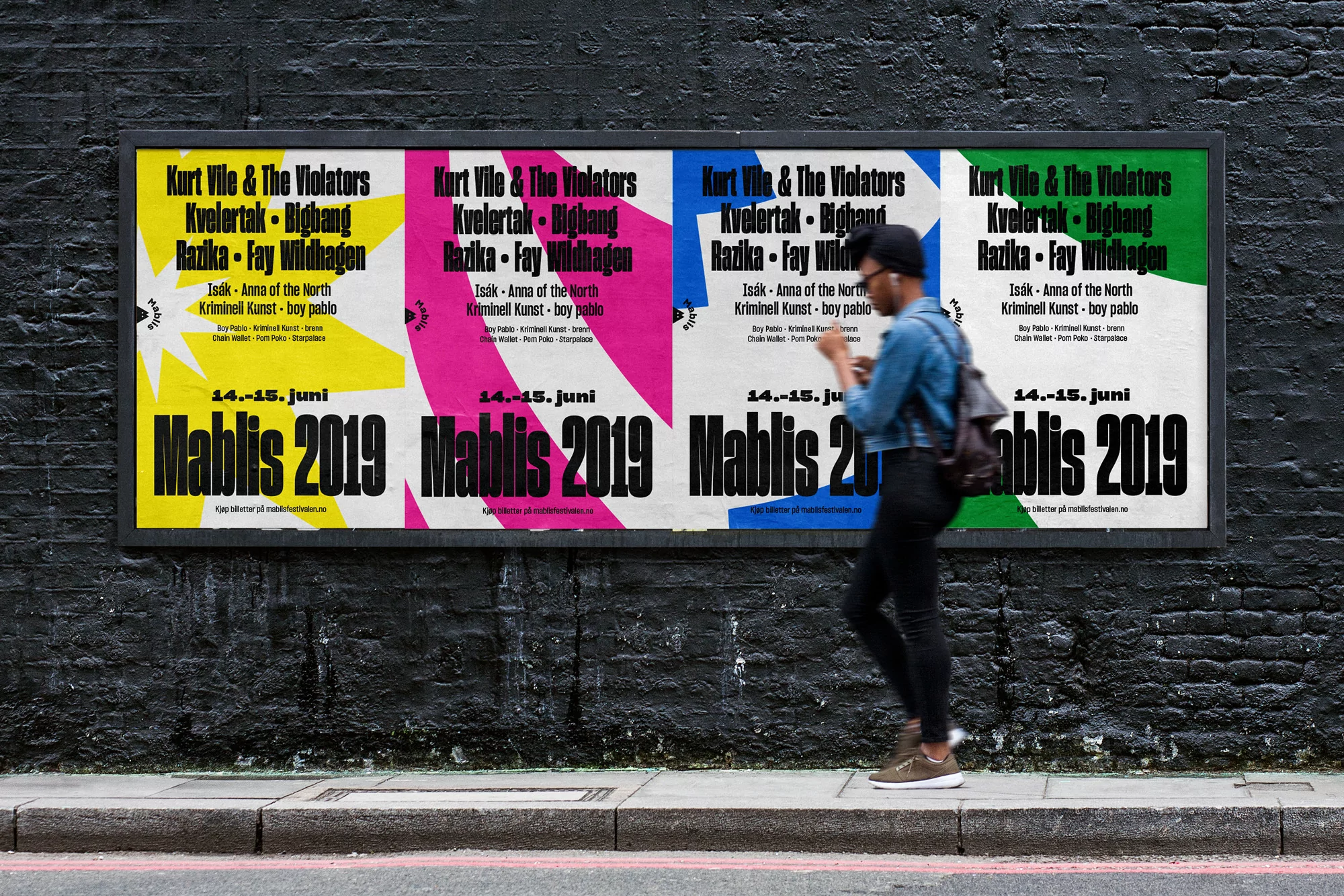 A person walks past a brick wall in an urban environment, where a large poster showcases colorful advertisements for a music event.