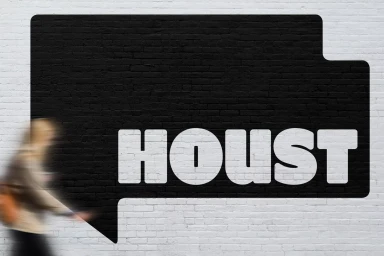 Houst brand identity logo painted black on a white brick wall with a blurred person walking past