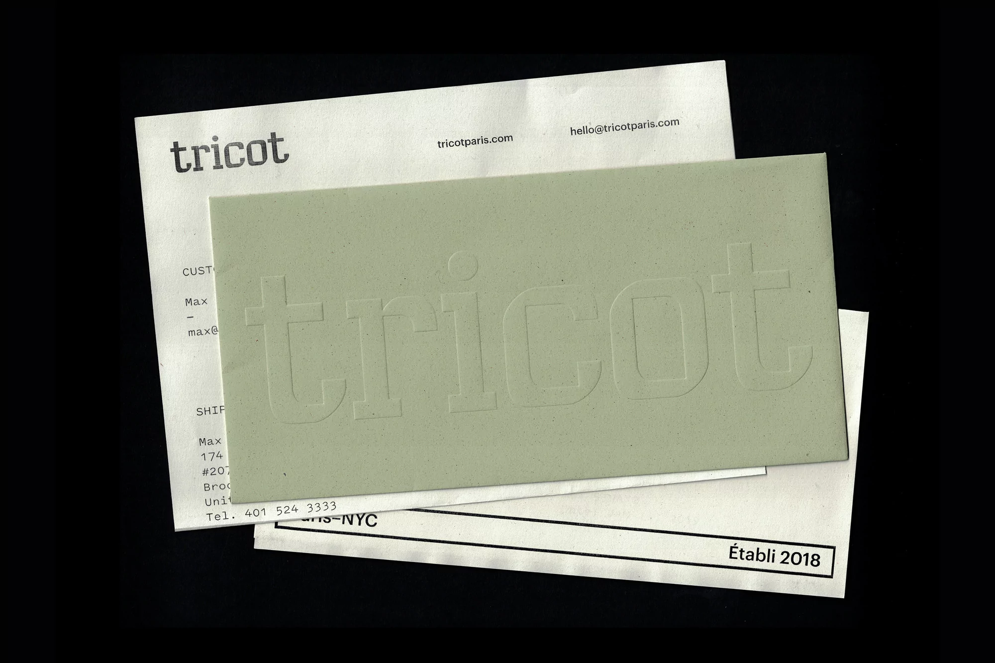 Close-up of stationery and business cards featuring the brand name 'tricot' in embossed lettering with soft, diffused lighting.